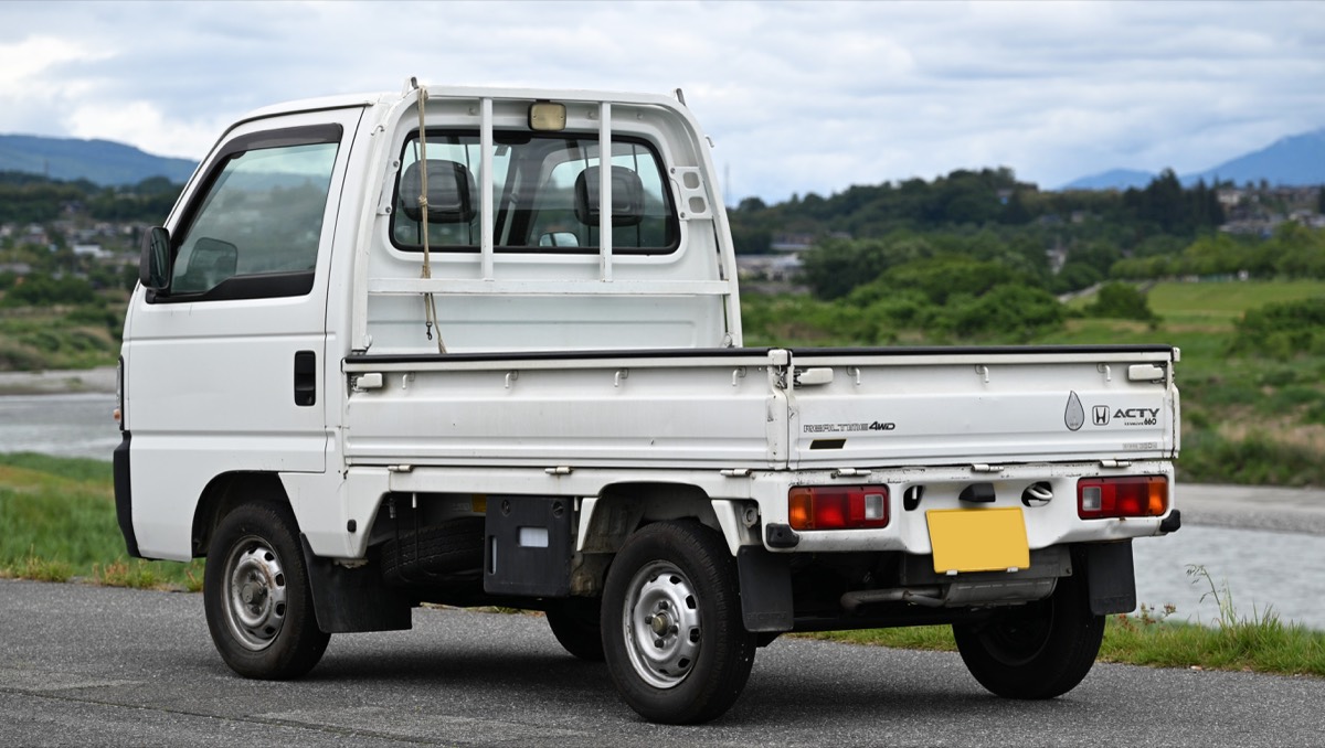 Rear three quarter view of a late 1990s Honda Acty SDX four wheel drive kei truck showing the flat bed with fold down sides