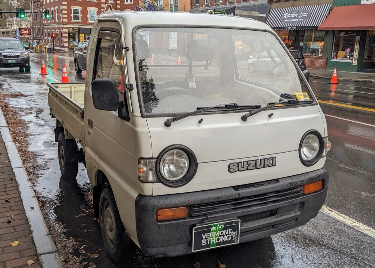 White Suzuki Carry kei truck parked on a rainy Main Street in downtown Brattleboro, Vermont